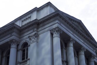 Fachada de um edifício neoclássico da Justiça, com colunas de mármore e detalhes arquitetônicos ornamentados.