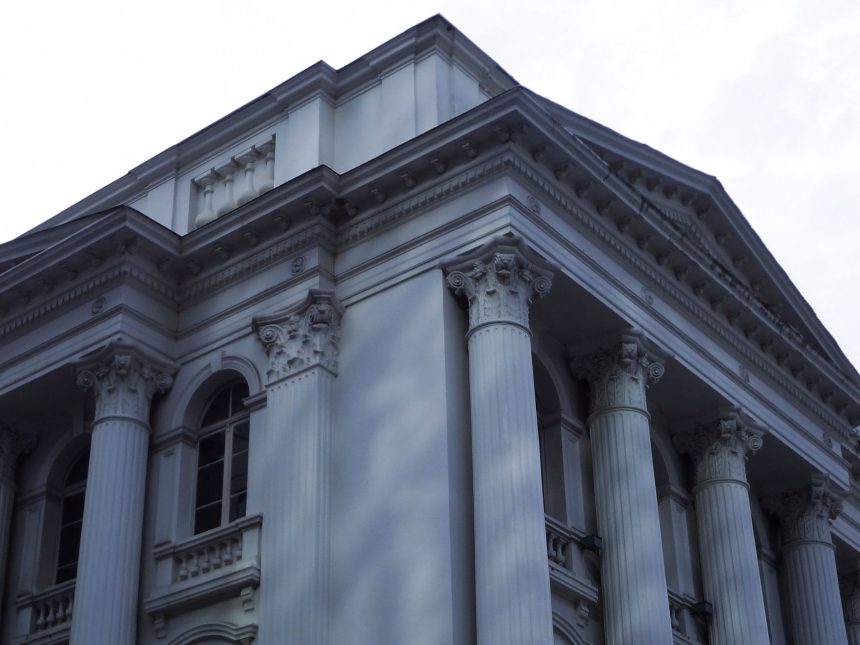 Fachada de um edifício neoclássico da Justiça, com colunas de mármore e detalhes arquitetônicos ornamentados.