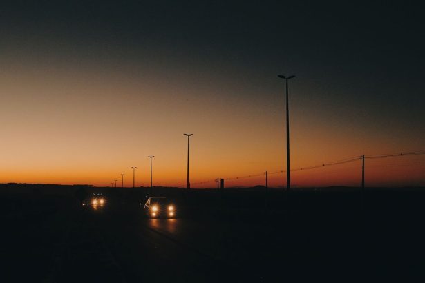 Rodovia com carros em circulação ao entardecer, postes de iluminação e linhas de transmissão ao longo da via.