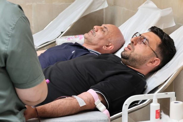 Dois homens doam sangue deitados em leitos de uma unidade de atendimento médico.