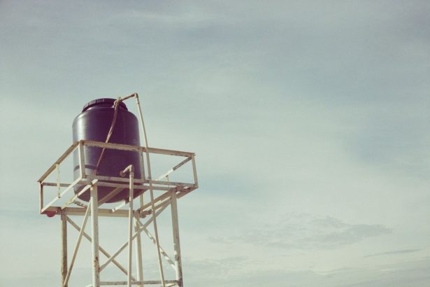 Reservatório de água industrial instalado sobre uma estrutura metálica, visto contra o céu azul.